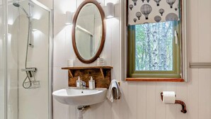 A bathroom with a glass shower enclosure, a wooden vanity with a mirror, and a window with a view of trees.