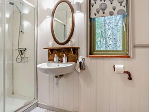 A bathroom with a glass shower enclosure, a wooden vanity with a mirror, and a window with a view of trees.