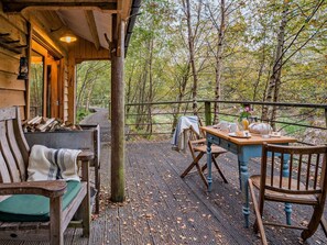 A wooden deck with a table and chairs, surrounded by trees.
