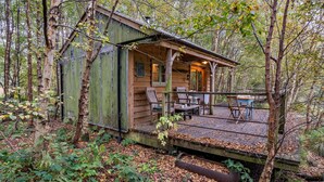 A rustic cabin with a porch, wooden deck, and seating area.