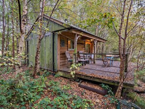 A rustic cabin with a porch, wooden deck, and seating area.