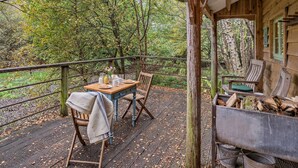 A wooden deck with a table set for two, surrounded by chairs, overlooking a forested area.