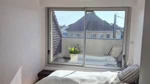 Et soveværelse med stor skydedør, seng, lille natbord, en potteplante og en loftlampe.