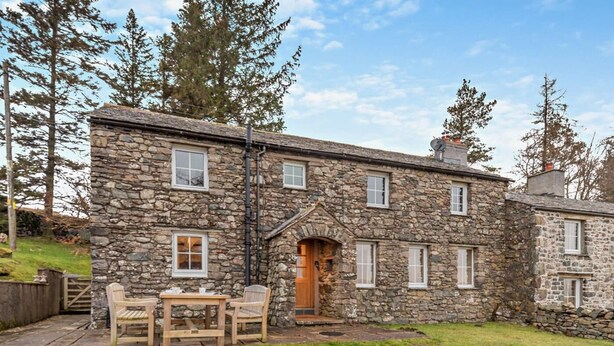 A stone house with a wooden door, a small patio with a table and chairs, and a grassy yard. - 3 Bed in Penrith (oc-sz247) (Dockray)
