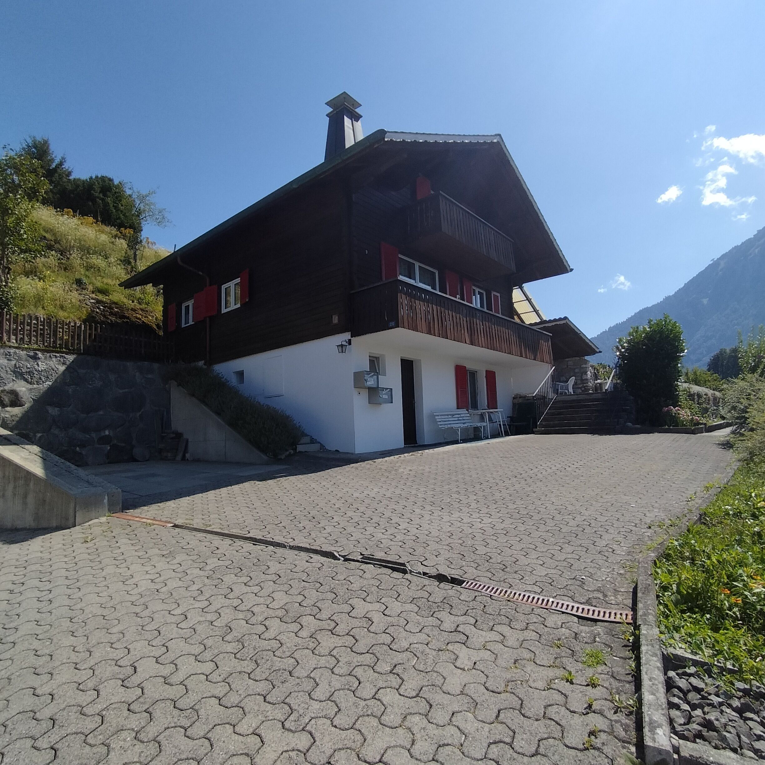 A two-story building with a sloped roof, a balcony, and a stone staircase leading to the entrance.