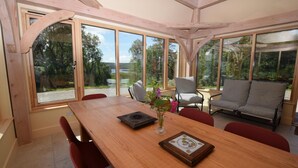 Ein Essbereich mit Holztisch, Stühlen und einer Couch. Große Fenster bieten Ausblick ins Freie.