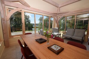 A dining area with a wooden table, chairs, and a sofa. Large windows provide a view of the outdoors. - 6 Bed in Lairg (oc-ca301) (West Shinness Lodge)