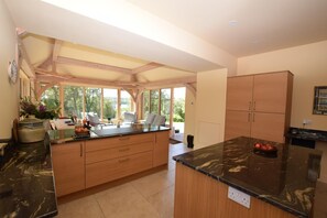 A kitchen with a large island, wooden cabinets, and a view through the windows. - 6 Bed in Lairg (oc-ca301) (West Shinness Lodge)