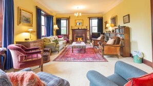 Ein traditionell eingerichtetes Wohnzimmer mit Kamin, verschiedenen Sitzgelegenheiten und einem Bücherregal.