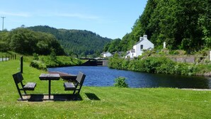 A riverside setting with a white building, a bridge, and a picnic table with benches. - 1 Bed in Lochgilphead (oc-ca304) (Lochgilphead)