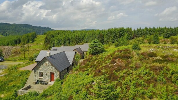 A stone house with a red door, surrounded by lush greenery and a forested hillside. - 1 Bed in Lochgilphead (oc-ca304) (Lochgilphead)