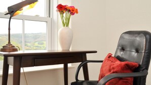 Een bureau met een lamp, een vaas met bloemen en een zwarte stoel met een rode kussen.