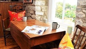 Een houten eettafel met een tijdschrift, twee gemêleerde mokken en een kleurrijk kussen.