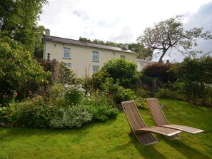 A house with a garden, two wooden lounge chairs, and a variety of plants. - 3 Bed in Llandovery (oc-76381) (Rhandirmwyn)