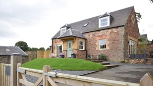 A stone house with a green door, a paved driveway, and a wooden gate. - 2 Bed in West Linton (oc-76383) (West Linton)