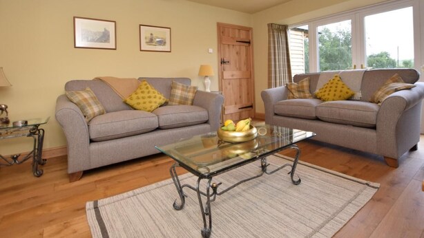 A living room with two grey sofas, a glass coffee table, wooden flooring, and a door with curtains. - 2 Bed in West Linton (oc-76383) (West Linton)