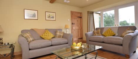 A living room with two grey sofas, a glass coffee table, wooden flooring, and a door with curtains.