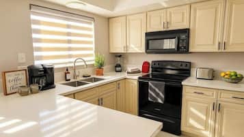 A kitchen with a coffee maker, microwave, toaster, and a bowl of fruit on the counter.