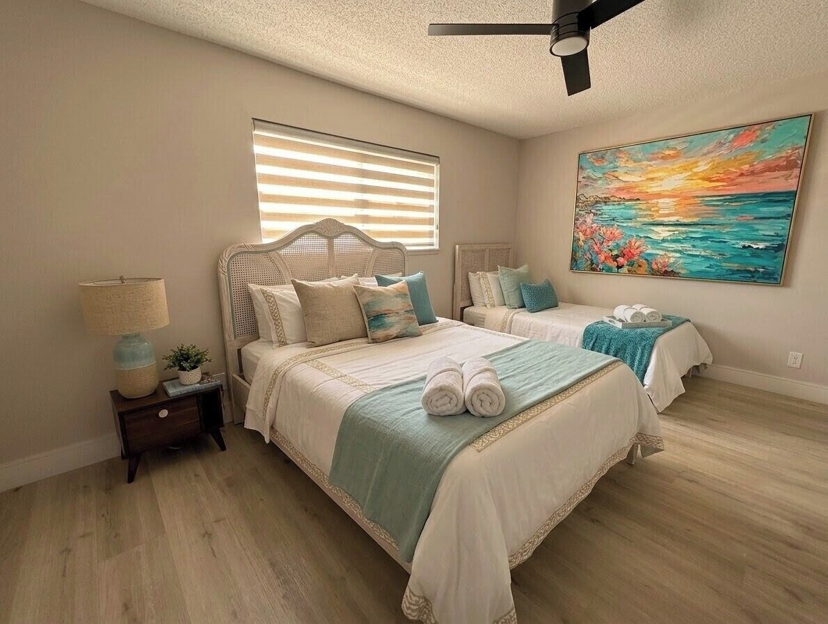 A bedroom with two beds, a ceiling fan, a painting, and a window with blinds.