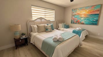 A bedroom with two beds, a ceiling fan, a painting, and a window with blinds.