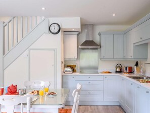 Una cocina moderna con gabinetes blancos, una campana extractora de acero inoxidable y un comedor con mesa y sillas de vidrio.
