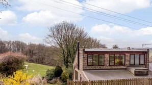 A stone building with a flat roof, large windows, and a wooden fence. - 1 Bed in Harrogate (oc-76511) (Summerbridge)