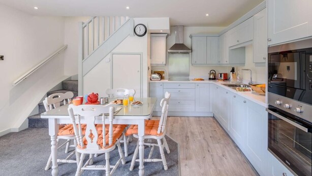 A modern kitchen with white cabinets, a built-in oven, and a dining area with a table and chairs. - 1 Bed in Harrogate (oc-76511) (Summerbridge)
