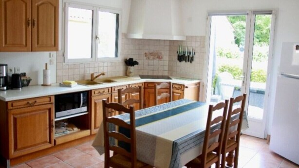 A kitchen with wooden cabinets, a dining table with chairs, a window, and a door leading outside. - Le Petit Balou Vacation Rental, Dordogne. A comfortable home near Bergerac (Lamonzie-Saint-Martin)