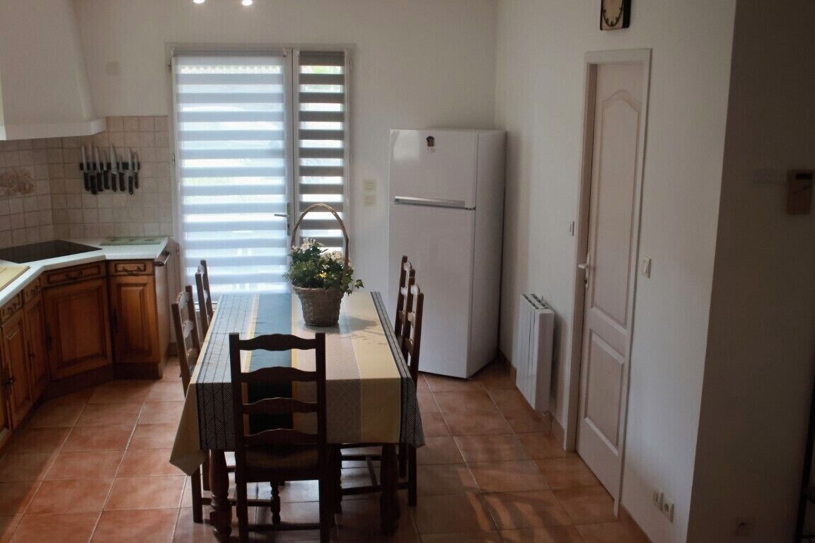 Eine Küche mit Esstisch, Stühlen, einem Kühlschrank und einem Fenster mit Jalousien.