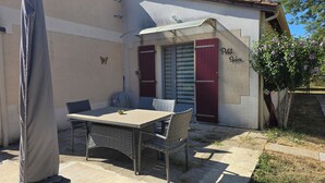 A patio with a table and chairs, a covered umbrella, a red door, and a wall with a butterfly decoration. - Le Petit Balou Vacation Rental, Dordogne. A comfortable home near Bergerac (Lamonzie-Saint-Martin)