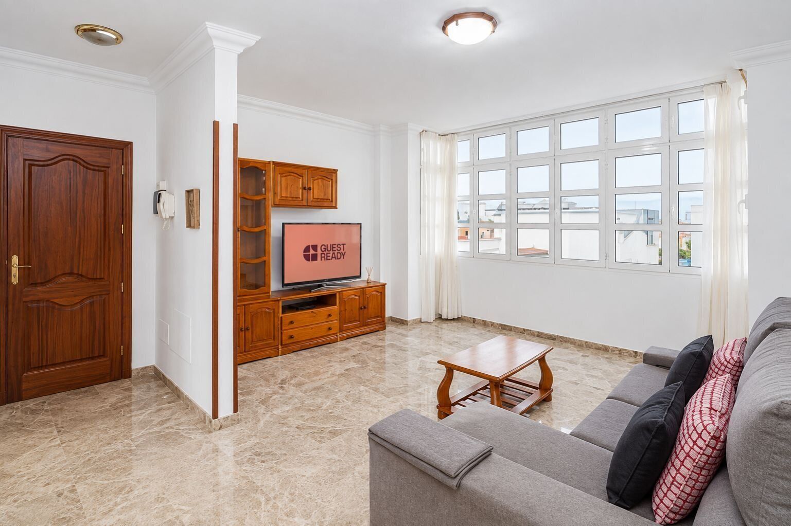 Een woonkamer met een bank, een televisie, een houten kast en een raam met uitzicht.