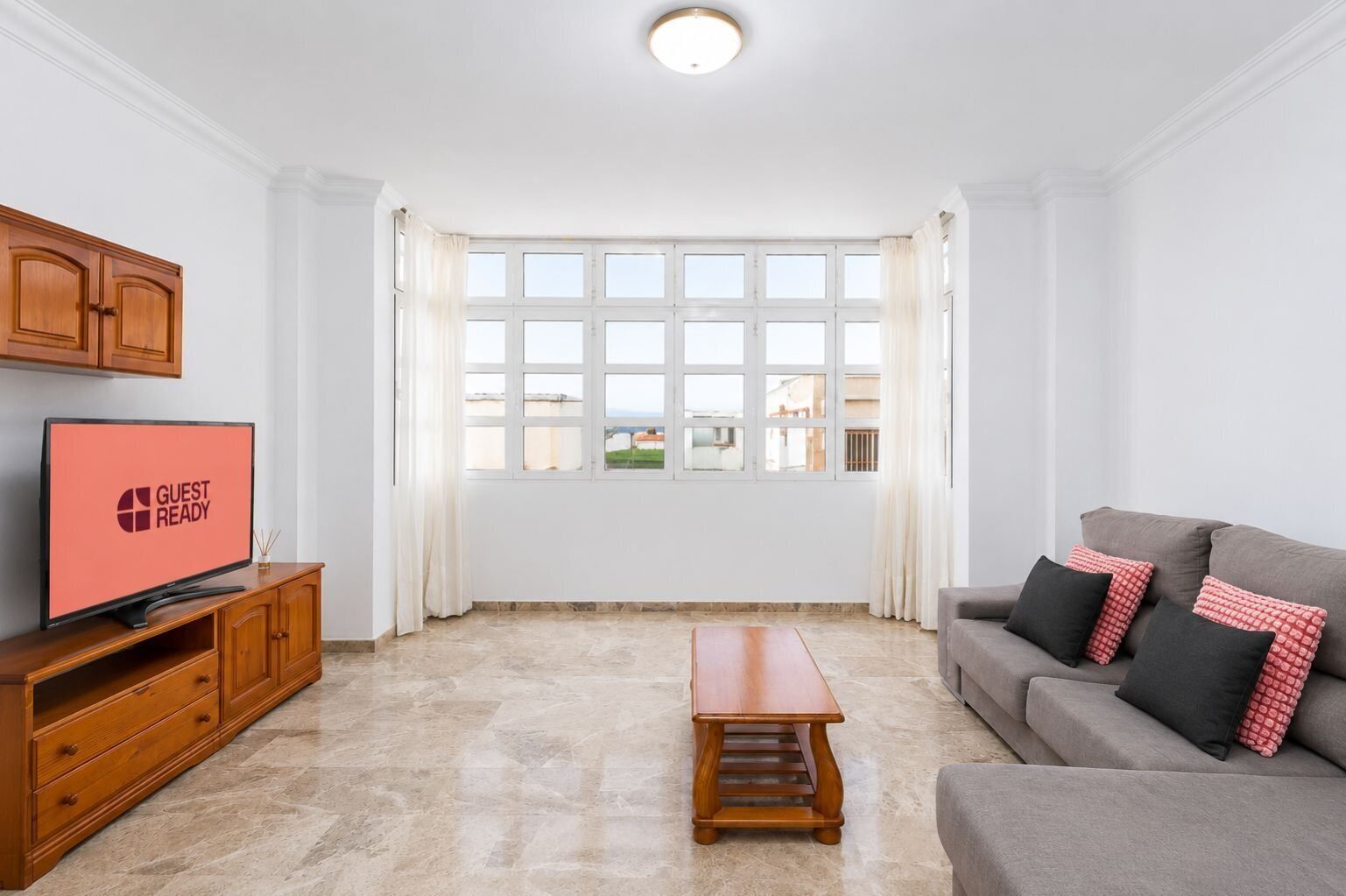 A modern living room with a television, a sofa, a coffee table, and a large window with curtains.