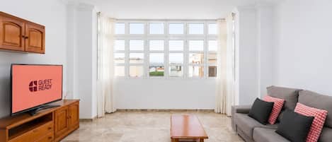 A modern living room with a television, a sofa, a coffee table, and a large window with curtains.