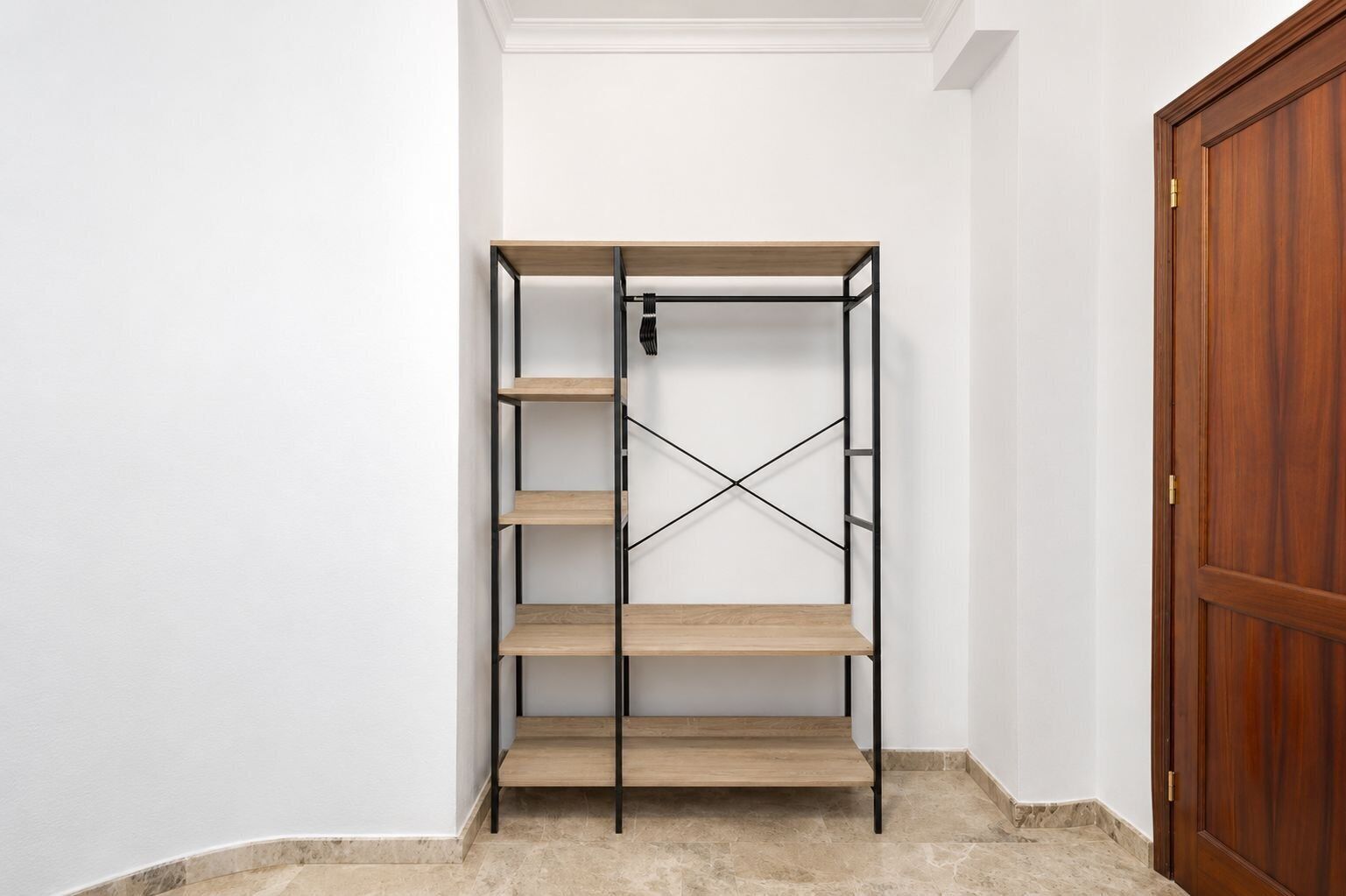 A corner room with a wooden wardrobe, a metal shelving unit, and a tiled floor.
