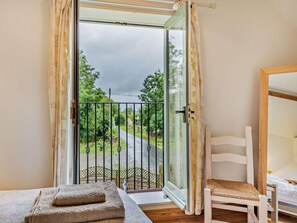 Ein Zimmer mit einem Bett, einem Sessel, einem Fenster mit Blick auf eine Straße und Grünflächen sowie einem Balkon mit Geländer.