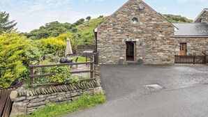 A stone building with a triangular roof, a wooden fence, and a paved driveway. - 3 Bed in Arthog (oc-77304) (Arthog)