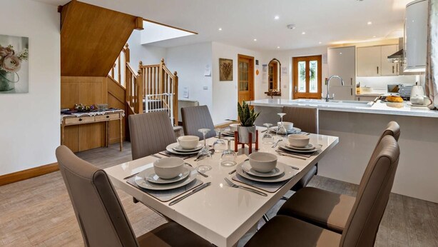 A modern kitchen with a central island, wooden staircase, and a dining area with a white table set for four. - 3 Bed in Arthog (oc-77304) (Arthog)