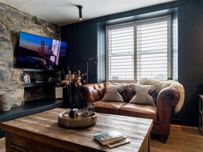 A living room with a stone wall, a leather sofa, a wooden coffee table, and a television mounted on the wall. - 3 Bed in Stranraer (oc-77308) (Portpatrick)