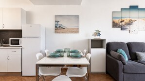 A modern kitchen with white cabinets and a microwave, a dining area with a white table and teal plates, and a gray sofa with teal cushions. - GuestReady - Tenesor Sun Beach Resort (Las Palmas de Gran Canaria)