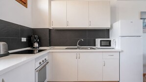 A modern kitchen with white cabinets, a stainless steel range, a microwave, and a refrigerator. - GuestReady - Tenesor Sun Beach Resort (Las Palmas de Gran Canaria)