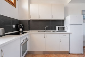 A modern kitchen with white cabinets, a stainless steel range, a microwave, and a refrigerator. - GuestReady - Tenesor Sun Beach Resort (Las Palmas de Gran Canaria)
