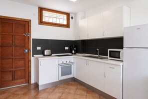 Eine Küche mit weißen Schränken, einer schwarzen Spritzschutzwand, einer Holztür, einem Fenster und einer Mikrowelle.