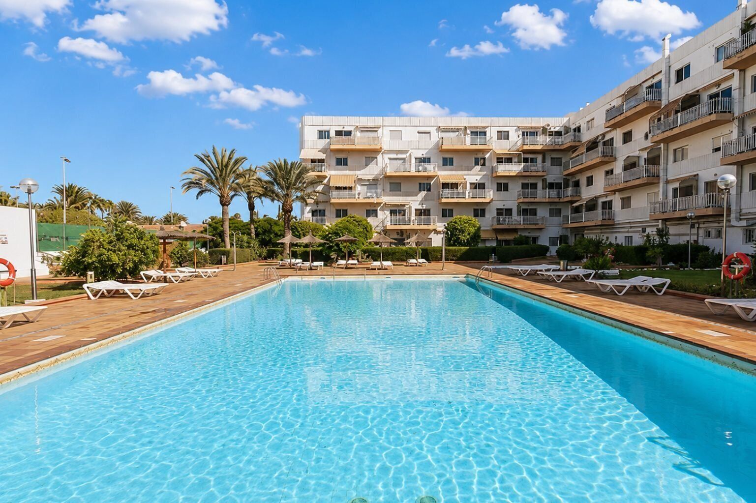 A swimming pool with lounge chairs and a multi-story building in the background.
