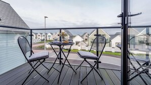 Ein Balkon mit zwei Stühlen, einem kleinen runden Tisch und einem Glasgeländer.