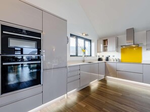 A modern kitchen with built-in appliances, a window, and a yellow accent wall. - 2 Bed in Bideford (oc-77289) (Northam)
