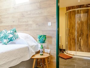 Ein Hotelzimmer mit einem Bett, einem kleinen Tisch mit einer Flasche, einer Lampe und einer Dusche.