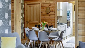 Interior em madeira com mesa de jantar posta para quatro, cozinha e sala de estar com sofá.