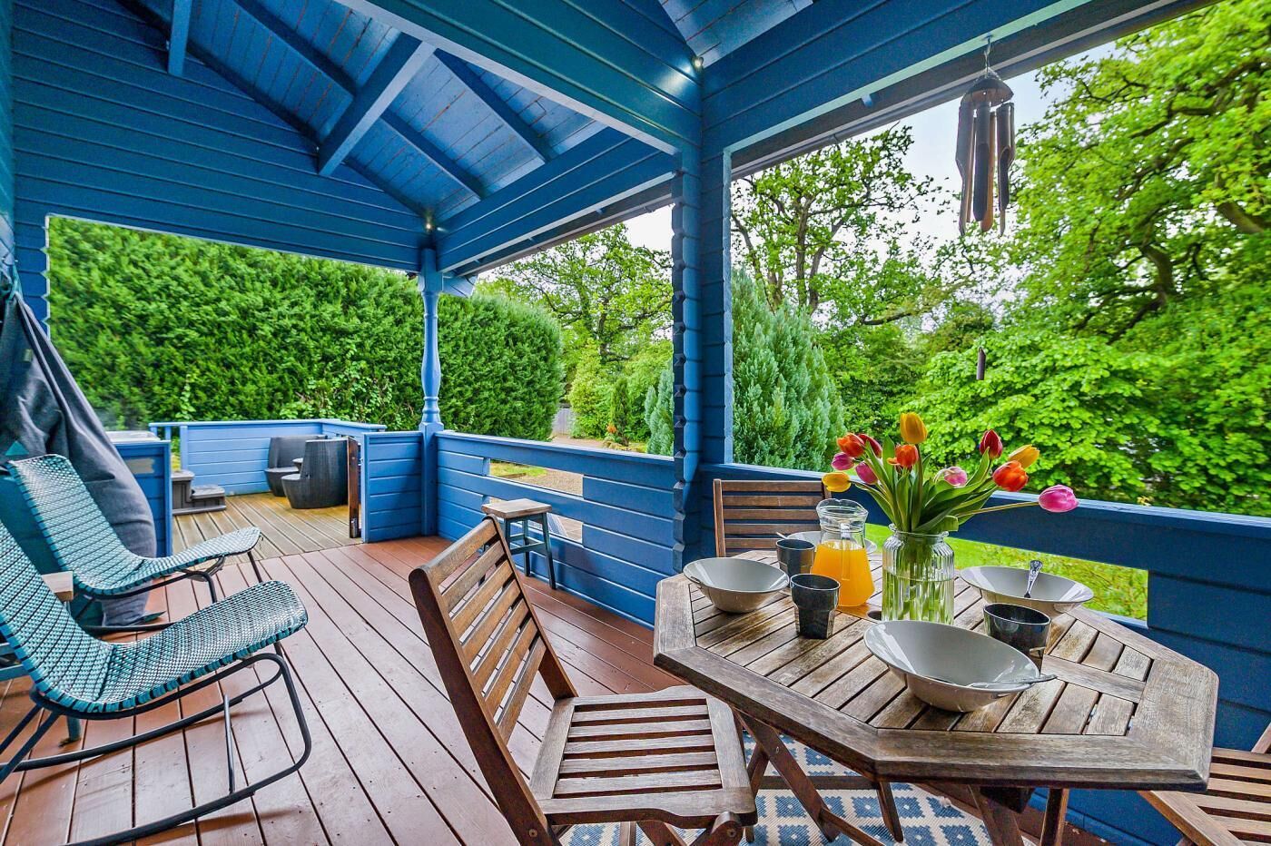 Eine überdachte Terrasse im Freien mit Holzmöbeln, einem für das Essen gedeckten Tisch und Blick ins Grüne.