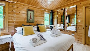 Quarto de cabana de madeira com cama, almofadas, um espelho e uma janela.