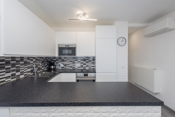 Uma cozinha moderna com bancada de granito preto, forno embutido e painel de azulejos.